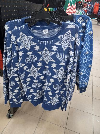 A picture of a Hanukkah sweater. It has menorahs, stars of David, and stars of David with snowflake inside them.