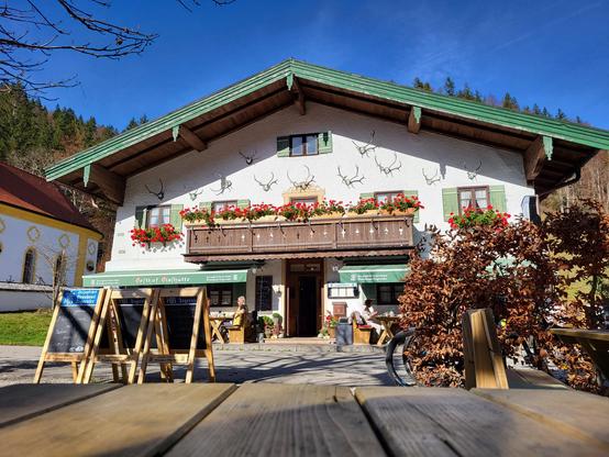 A detailed image of a building with a balcony and a sign is captured in this photograph. The building features a brown exterior with a blue sky in the background. There are trees and plants surrounding the building, adding a touch of greenery to the scene. The balcony is visible on the upper level, and there is a sign displayed prominently on the front of the building. The overall atmosphere is serene and inviting, with a hint of a cloudy sky above. The architecture is a mix of modern and traditional elements, providing a unique and charming aesthetic.