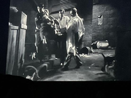 Mike Mazurki and two other burly guys dragging a limp Burt Lancaster into an alley filled with trash and three cats in a black and white movie scene