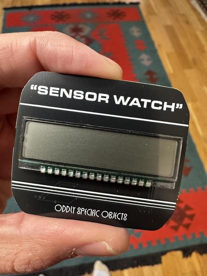 Photo of a small gadget with a screen. Text on the gadget reads “Sensor Watch” in quotes. 