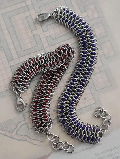 two bracelets made with the dragonscale chainmaille weave. both are made primarily with stainless steel rings, the the inner color varies between the two. one is red with black and the other is purple with green.