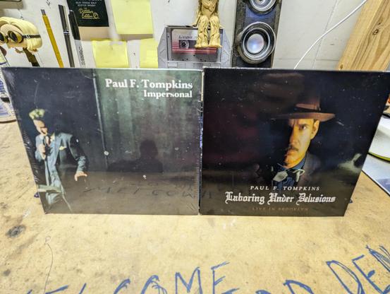 2 CD albums of Comedian Paul F. Tompkins take on garage workbench