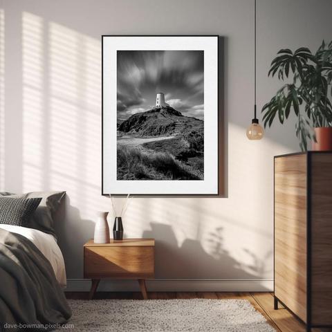 This monochrome long exposure photograph of Twr Mawr Lighthouse is elegantly framed and displayed on the wall of a modern bedroom. It features the steps leading up to the historic lighthouse on Llanddwyn Island in Anglesey, North Wales. The dramatic sky above showcases streaking clouds, adding a dynamic sense of movement to the scene. The lighthouse stands as a strong focal point, inviting viewers to imagine the journey up the steps. The artwork, titled "Tŵr Mawr Lighthouse," enhances the room's contemporary aesthetic while offering a serene connection to the coastal landscape.