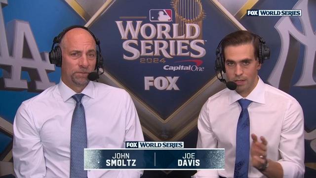 The image shows two commentators, John Smoltz and Joe Davis, seated in a broadcast booth during the 2024 World Series. They are wearing headsets and discussing the game, with the World Series logo prominently displayed behind them.