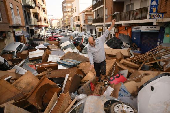 Photographs of the floods in Spain: A man walks over the cars, garbage and debris washed away by floodwaters