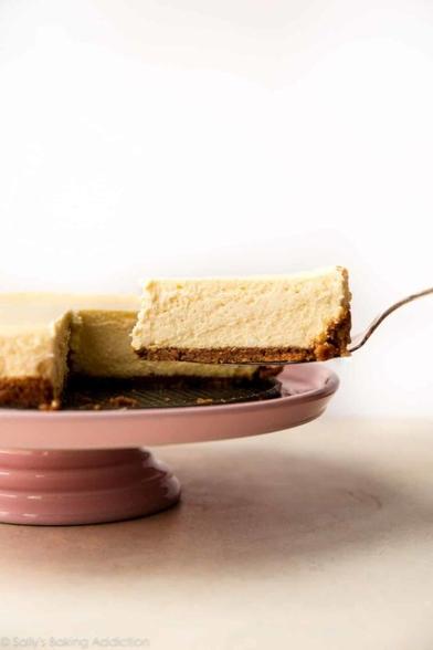 An inviting image of a slice of plain cheesecake being cut from the whole cheesecake.