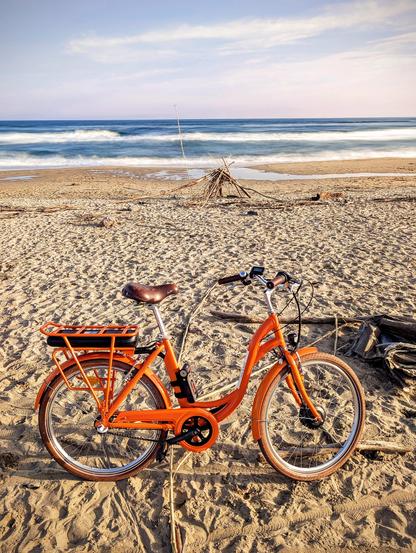 Un vélo de location orange sur la plage de Sète. La mer en arrière plan en pause longue