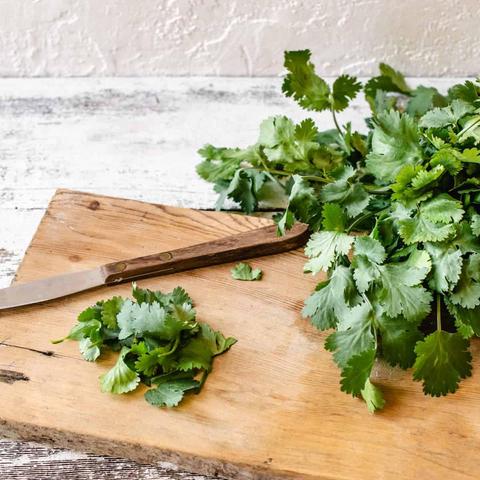 An image of fresh cilantro ... sitting on a cutting board with a small knife that's there. A small bunch of it is ready to be chopped slightly & then, added to a favorite dish like guacamole.