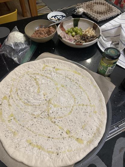 Ingredients for a pizza arranged around a stretched pizza dough. 