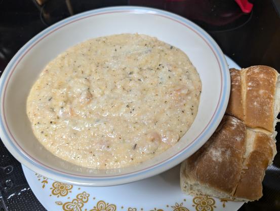 Bowl with creamy grits and small shrimp, and rolls on the side.