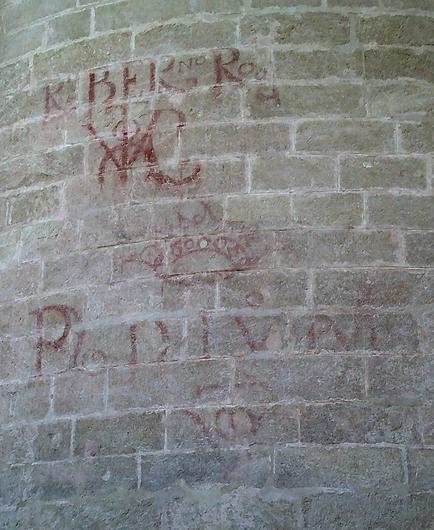 Muro de la catedral de Sevilla con símbolos rojos del vítor y los nombres, normalmente abreviados.