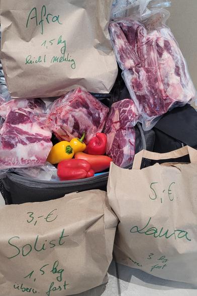 Foto der eingekauften Produkte: drei Papiertüten mit Kartoffeln, Sorten: Afra, Solist und Laura, dazwischen eine offene Kühltasche mit vakuumierten Fleischteilen und ein paar roten und gelben kleinen, spitzen Paprika. 