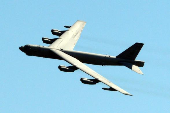 A B-52 Stratofortress aircraft performing a fly-by at AirVenture 2008. The aircraft is seen from a side angle against a clear blue sky, showcasing its large wingspan and eight engines mounted in pairs under the wings.