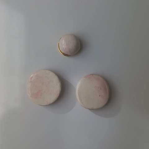 Foto en la que se muestran 3 imanes marmolados blancos y rosas pegados a una nevera.