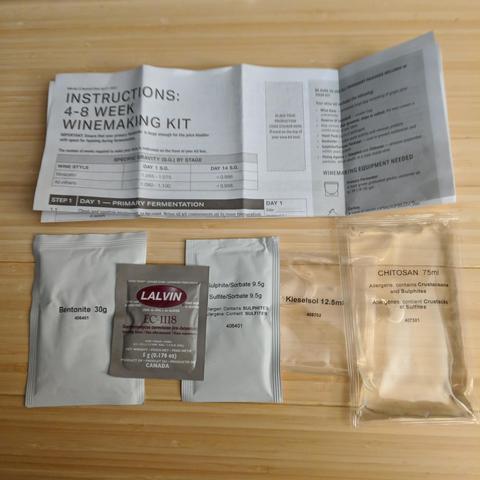 A square cropped photo showing the instructions paper, and from left to right a pouch of bentonite 30g, lalvin ec-1118 yeast, sorbate 9.5g, kieselsol 12.5ml, and chitosan 75ml. They are laid out on a custom made bamboo countertop constructed by the photographer.