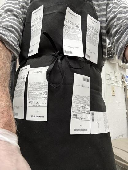 Closeup of a man wearing a black apron with labels arranged on the front