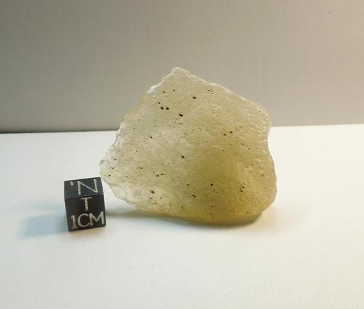 A small gemmy piece of Libyan Desert Glass next to a black centimeter scale cube.