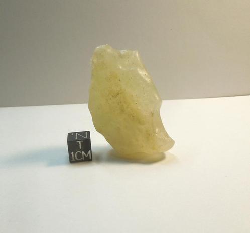 A small gemmy piece of Libyan Desert Glass next to a black centimeter scale cube.