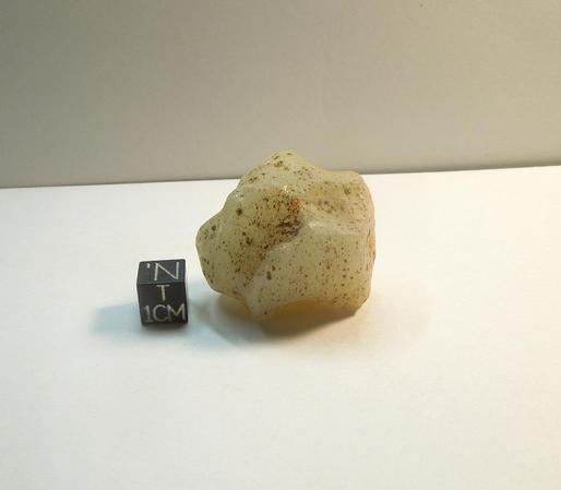 A small milky piece of Libyan Desert Glass next to a black centimeter scale cube.