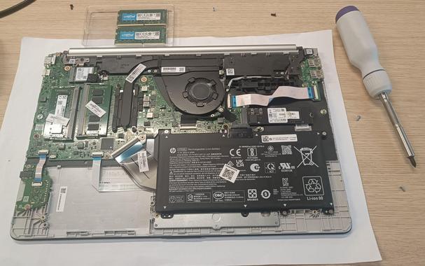 Second laptop without its bottom cover, exposing all of the internals, namely the RAM slots with their original 2x8 memory kit from factory, which are about to be replaced with the 2x16 kit that was in the first laptop