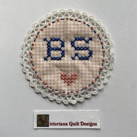 Circle with cross-stitched initials & heart. 