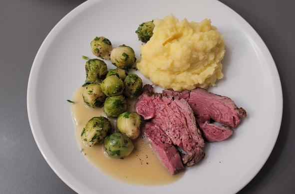 Farbfoto: Auf einem weißen Teller liegen zwei Stücke Filet, außen angebraten, innen ungefähr zwischen rare und medium rare, dazu der Kartoffelstampf und Rosenkohl, leicht geröstet und mit Petersilie daran. Ein wenig helle Sauce aus Fond und Weißwein ist auch noch dabei. 