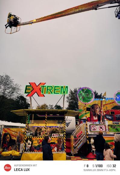Kassenhaus des Karussels „Extrem“. Eine Gondel ist am oberen Bildrand zu sehen. Ein Passant schaut nach oben zu der Gondel, die nicht im Bild ist
