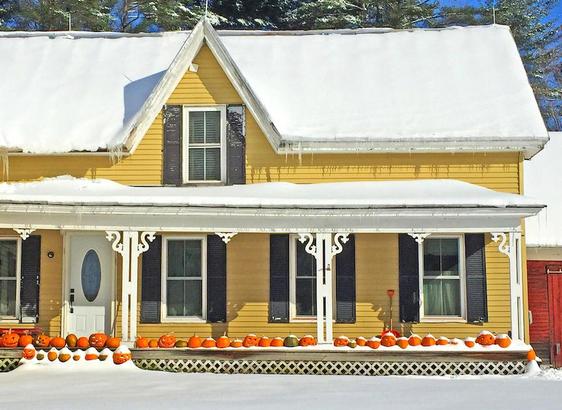 A row of pumpkins on a farmhouse porch in the snow.