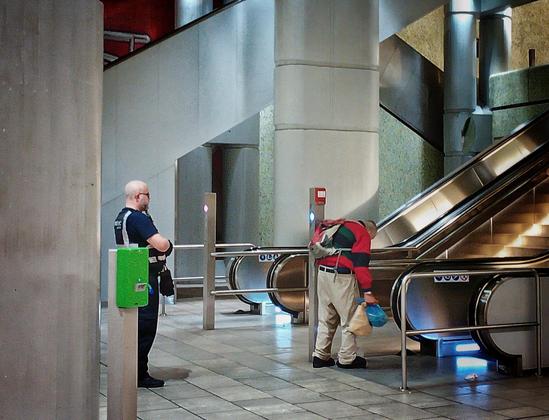 Foto zeigt den Rauswurf eines Obdachlosen, Hannover, Kröpcke. Der alte Mann ist gebrechlich. Er hat Mühe, seine Sachen unter Kontrolle zu bringen, die Rolltreppe zu betreten. UBahnhof ist Wärme, Trockenheit, unter Menschen sein bedeutet Sicherheit, hier gibt es wenigstens noch Sitzgelegenheit. Den "Sicherheits"-Nazis von Protec ist das egal: sie zeigen kein Verständnis für Artikel 1 Grundgesetz.