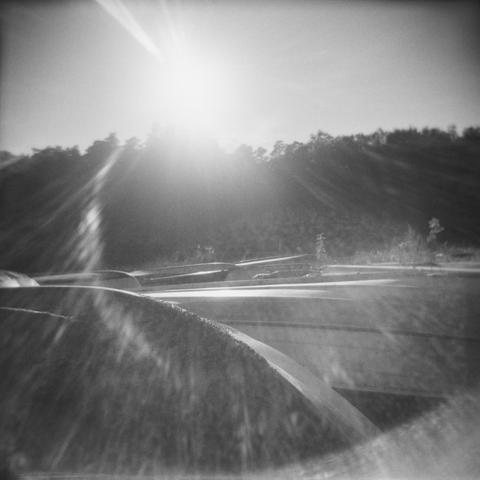 The sun shining over boats laid up on the shore for winter. Blurry forest background and the sun visible in the sky with rays created by the poor quality lens.