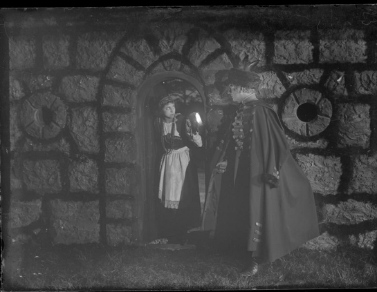 an image from the movie, a man holding a small lantern coming to the door of a worried looking young lady, the building stone