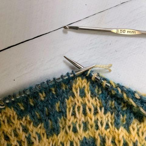 Close up of a mosaic project in yellow and teal yarn. Loose stitches are all fixed.