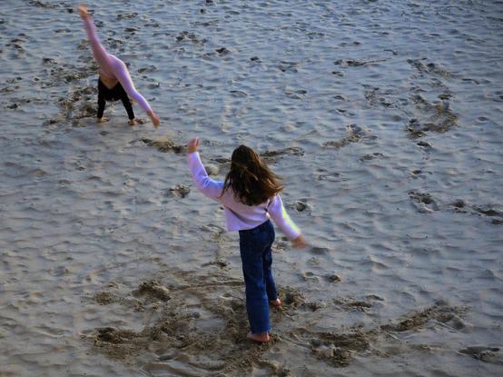 Dos niñas juegan en la playa, dando volteretas, al caer la tarde.