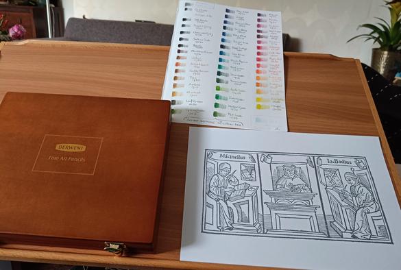 Colouring print of three seated men: two writing one reading. Writers are profile, reader is frontal. Latin text "Macinellus. Io. Badius"
Box of Derwent fine art pencils and test sheet of each colour.
All on a wooden mobile table