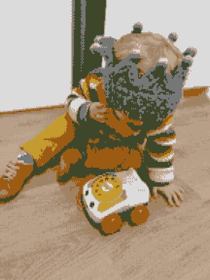 A child wearing a crown-shaped hat is sitting on the floor, playing with a toy phone. The child is dressed in orange and striped clothing.