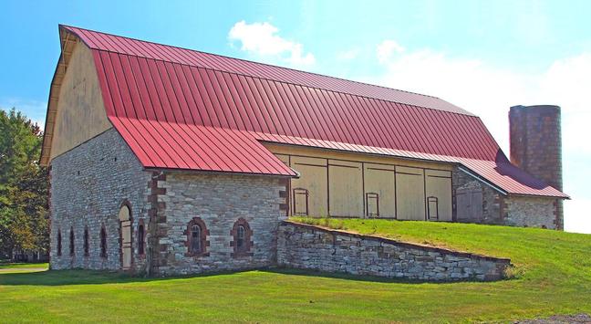 A large stone barn with a red metal roof on a bright sunny day.