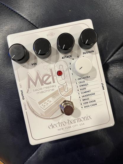 An Electro-Harmonix Mel9 tape replay machine pedal featuring various control knobs for volume, effect, attack, and sustain, along with a selection of instrument settings that replicate a melotron. The pedal is positioned on a dark textured surface.