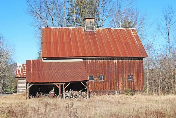 A weathered old barn has a very rusty metal roof.