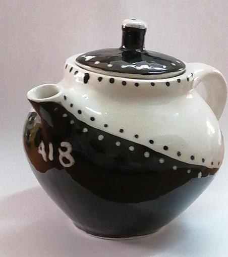 A small ceramic teapot, onliquely black on the bottom, white on top, with a black lid, and contrasting spots along the boundaries.
Under the spout, the numbers 418