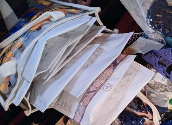 A bag overflowing with large white envelopes, surrounded by a mess of gift boxes, scissors, packaging materials and other, unfilled envelopes.