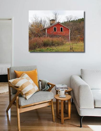 A frameless photo of an old red barn hangs on the wall above a chair and small table.