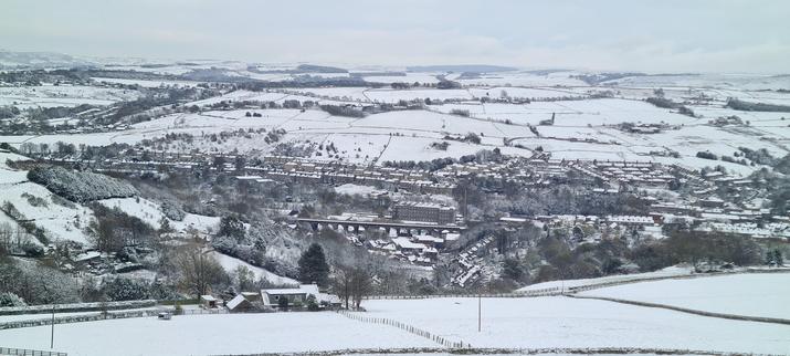 A boring photo that doesn't include any puppies. It's a long distance landscape picture, over a village set in a valley. All the hills are covered in snow but details can be picked out - trees and walls mostly. In the village, along with the assorted houses etc, there's an old stone viaduct with majestic arches, and beyond that, an old stone textile mill.