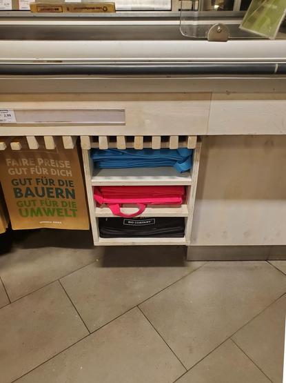 Hellblaue und pinke Einkaufsbeutel in einem Regal unter dem Kassenband im Supermarkt