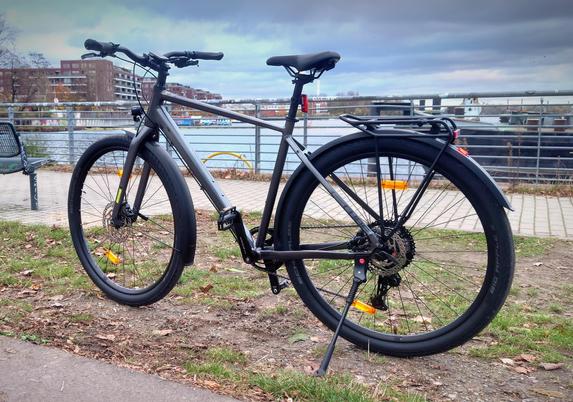 Ein graues Fahrrad steht auf dem Seitenständer, man sieht die linke Seite. Im Hintergrund die Rummelsburger Bucht. 