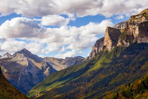 Fotografía donde se ven un par de formaciones montañosas con faldas de vegetación con colores de otoño. En la parte superior se pueden ver un cielo azul con nubes.