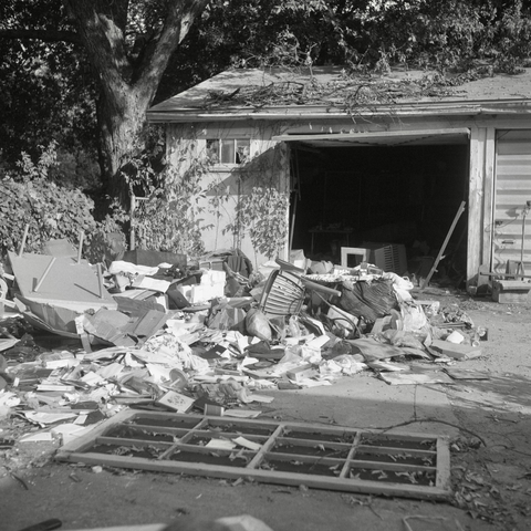 A black and white film photo. The personal belongings that were stored inside an abandoned garage are now scattered in front of it with its garage door wide open in East Austin, Texas. Wednesday, October 16, 2024.