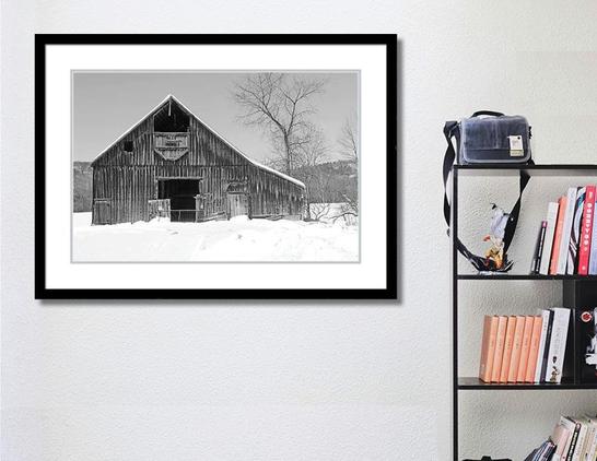 A framed photo of an old barn in winter hangs on a wall by a bookcase.