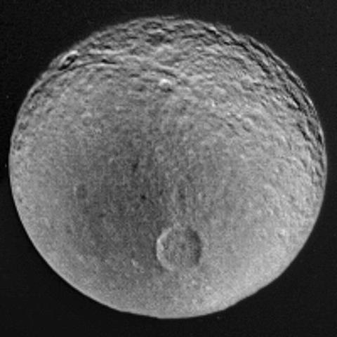 A Voyager 2 image of Tethys, moon of Saturn. Craters are visible, especially around the top of the disk. A dark patch occupies much of the left side. Below the middle of the image is a very prominent large crater called Penelope.