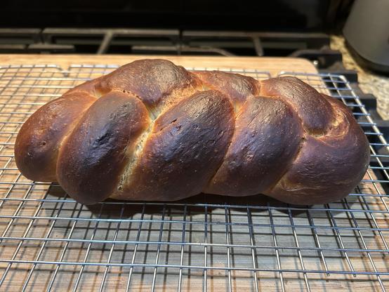 Yummy-looking braided baked cardamom loaf on a cooling rack on top of a cutting board. I adapted her recipe for use in the bread machine.
Recipe:
Makes two loaves
Ingredients

• 1 egg in 2 C measuring cup
• Milk to make 1 1/4 C when added to egg
• 2 T unsalted butter
• 1/2 t salt
• 1/3 C sugar
• 1 t cardamom
• 3 C unbleached white bread flour
• 1/4 C raisins or dried cranberries
• 2 1/4 t dry yeast
• ½ t powdered egg or 1 beaten egg


Directions (Order is according to my bread machine. Yours may differ.)

Put liquid ingredients and butter in bread machine. Add dry ingredients except for dried fruit. Start bread machine and add dried fruit around edges after machine has run for a while or place in dispenser at beginning of cycle or knead in after machine is finished. When dough cycle is finished, form into two braids or one large loaf, wash with dried egg mixed with small amount of water, beaten egg or milk. Allow to rise for approximately 30 minutes.

Bake at 400° F for 25 minutes, or until nicely browned on top.

Note: In Finland, this bread is traditionally served with coffee for guests.