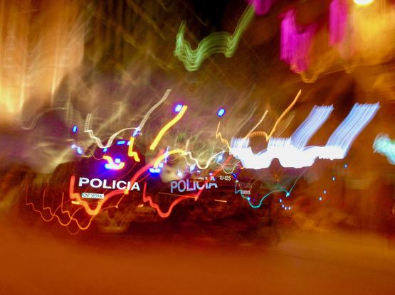 Foto nocturna en la que aparecen ráfagas de luz movida en la que todo aparece borroso y caótico excepto los rótulos de dos motos de  la policia, que es lo único que se puede ver con nitidez.